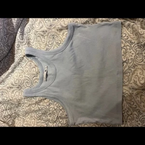 Ljusblå ribbad linnetopp 157 - Säljer en ljusblå croppad linnetopp från 157. Toppen är ribbad och har breda axelband samt rundad halsringning. Perfekt för varma dagar eller som lager under skjorta. Enkel och stilren design som är lätt att matcha.