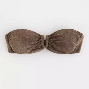 Glittrig bandeau bikiniöverdel brun - Snygg bandeau bikiniöverdel i glittrigt brunt tyg med gulddetaljer framtill. Modellen har rynkade kupor ochbhsr justerbar passform med knytte.