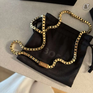Guldfärgat halsband från BOSS - Stilrent halsband från BOSS i guldfärgad metall med fyrkantiga länkar och diskret BOSS-logga på en bricka. Kedjan har en modern och chunky känsla, perfekt för att lyfta din outfit. Levereras i originalask med tillhörande påse och märkning. Den är helt oanvänd så i nyskick! 