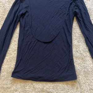 Svart långärmad topp från Missay - Svart långärmad topp från Missay med djup, rundad öppen rygg. Toppens material är mjukt och stretchigt, perfekt för en stilren look. Passformen är tight och den har en enkel, minimalistisk design utan mönster eller extra detaljer. Kontakta för fler bilder🩷