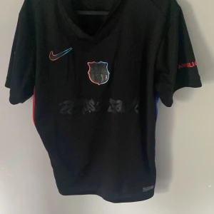 FC Barcelona Raphinha 11 Nike tröja - Snygg svart FC Barcelona fotbollströja från Nike med Raphinha och nummer 11 på ryggen. Tröjan har röda och blå detaljer på sidorna, klubbmärke och Nike-logga framtill samt tryck på ärmen. Perfekt för dig som älskar Barca och vill sticka ut på match eller träning.