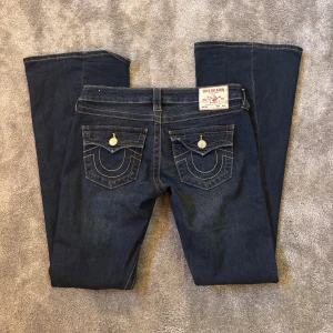 True Religion Joey Low Rise Flare Jeans - Mörkblå jeans från True Religion, modell Joey Low Rise Flare. Snygga kontrastsömmar, klassiska fickor med lock och silverfärgade knappar. Bootcut/flare passform och låg midja. Mycket fint skick enda defekten är vid längst ner på benen, se bild💞