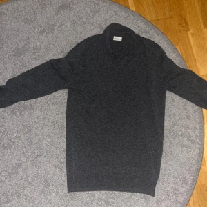 Mörkgrå kashmir tröja med krage John Henric  - Säljer en mörkgrå Kashmir tröja från John Henric i storlek S. Tröjan har klassisk krage och lång ärm, perfekt för lager-på-lager. Materialet är mjukt och ger en clean och stilren look. Passar dig som gillar enkel och tidlös stil. 