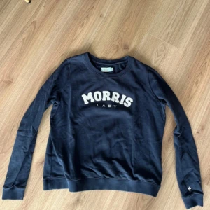 Mörkblå sweatshirt från Morris Lady - Mörkblå sweatshirt från Morris Lady med vit broderad logga framtill. Tröjan har rund halsringning, långa ärmar och ribbade muddar. Tillverkad i mjuk bomull för en skön känsla. Perfekt för en avslappnad och stilren look.