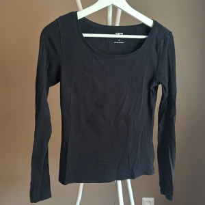 Svart långärmad topp från 157 - En basic svart långärmad topp från 157 i mjuk bomullsblandning med lite stretch. Enkel och stilren design med rund halsringning, perfekt att matcha med jeans eller kjol. Materialet är 95% bomull och 5% elastan.🌸