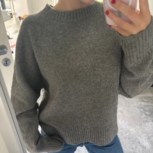 Grå stickad tröja från Zara - Mysig grå stickad tröja från Zara med rund halsringning och ribbade muddar vid ärmslut och nederkant. Tröjan har en loose passform och är perfekt för kyliga dagar. Enkel och stilren design som funkar till allt.