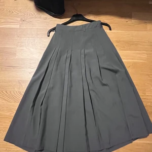 Grå långkjol från WUZHINVHAI - Säljer en snygg grå långkjol från WUZHINVHAI. Kjolen har klassiska veck framtill och en diskret dragkedja i sidan. Den är i ett mjukt och följsamt material som ger ett stilrent intryck. Perfekt för dig som gillar minimalistisk och clean stil. Passar mer XS S