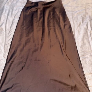 Brun långkjol i satin från Lindex - Säljer en snygg brun långkjol från Lindex i satin material. Kjolen har en stilren och enkel design med lätt glansig yta som ger en lyxig känsla. Perfekt att styla med en stickad tröja eller en cool topp.