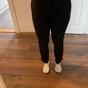 Svarta kostymbyxor med slits - Svarta kostymbyxor med hög midja och raka ben. Byxorna har slits vid benslut, bälteshällor och två fuskbakfickor. 