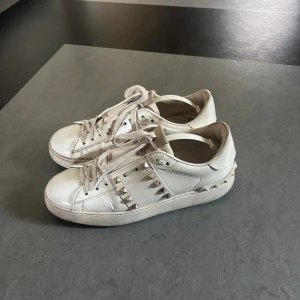 Valentino Rockstud vita sneakers - Snygga vita Valentino Rockstud sneakers i skinn med ikoniska nitar i  guld längs sidorna. Äkta men har inte kvar äkthetsbevis eller kartong tyvärr, okej skick därav priset 🥰