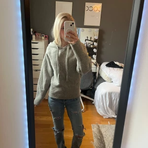 Grå stickad hoodie med huva - Mysig grå stickad hoodie med huva och snörning framtill. Tröjan har breda ribbade muddar vid ärmslut och nederkant, samt långärmad passform. Perfekt för dig som gillar en chill och enkel stil.