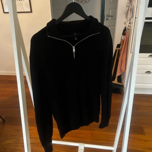 Svart stickad half zip-tröja H&M - Svart stickad tröja från H&M med regular fit och half zip-dragkedja framtill. Tröjan har en hög krage och långa ärmar, perfekt för att hålla värmen under kyliga dagar. Enkel och stilren design som funkar till många olika looks.