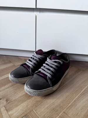 Lanvin sneakers i vinröd mocka - Säljer ett par snygga Lanvin sneakers med vinröd mocka och grå snörning. Skorna har rund tå i blank grått skinn och vit platt sula. Klassisk låg modell med lyxig känsla och cool färgkombo som sticker ut. Skriv gärna vid fler frågor! 