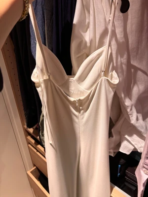 Champagnefärgad långklänning med snörning - Säljer en elegant vit långklänning med tunna axelband och snygg drapering längs sidan. Klänningen har snörning som ger en cool rynkad effekt och en feminin siluett. Materialet känns mjukt och har ett lätt fall. Dragkedja i ryggen för enkel påklädning.