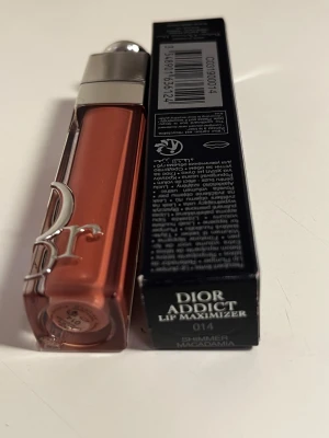 Dior Addict Lip Maximizer Shimmer Macadamia - Dior Addict Lip Maximizer i färgen 014 Shimmer Macadamia. Ett lyxigt läppglans med volymgivande effekt och skimrande finish. Färgen är en varm nude med subtilt guldskimmer. Snygg förpackning med silverlock och Dior-logga i metall på genomskinlig plast.