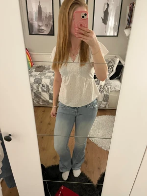 Vit blus med spets och v-ringning - Säljer en söt vit blus med korta ärmar och v-ringning. Blusen har broderade spetsdetaljer runt halsen och ett hålmönster över hela tyget. Den är lätt utsvängd nedtill och har en feminin, luftig känsla. Perfekt för dig som gillar romantisk och fräsch stil.