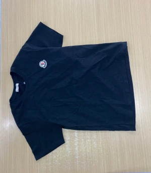 Svart t-shirt från Moncler med logga - Svart t-shirt från Moncler med klassisk rund hals och korta ärmar. T-shirten har Monclers ikoniska logga broderad på bröstet. En clean och stilren tee som passar perfekt till jeans eller shorts.