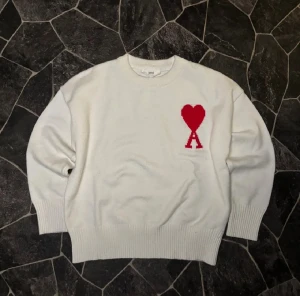 Vit stickad tröja från Ami med hjärta - Pris kan diskuteras ! Vit stickad tröja från Ami med rund hals och ribbade muddar. På bröstet finns ett rött hjärta med bokstaven A, vilket ger en unik och snygg detalj. Perfekt för dig som gillar stilrena plagg med en twist.