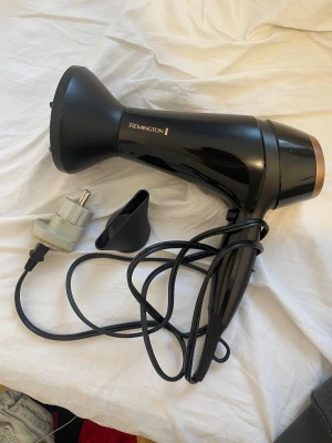 Remington hårfön - Remington hårfön i svart med två munstycken och strömadapter. Fungerar utmärkt och är helt oanvänd. Perfekt för både volym och styling. Passar europeiska eluttag med medföljande adapter.