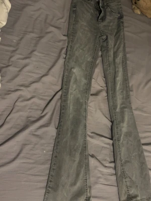 Grå bootcut jeans från ONLY - Snygga grå jeans från ONLY med bootcut-modell och hög midja. Jeansen har klassiska fickor, bälteshällor och dragkedja med knapp. Perfekta för dig som gillar en retroinspirerad look med lite utsvängda ben. Materialet är mjukt och följsamt jeans.