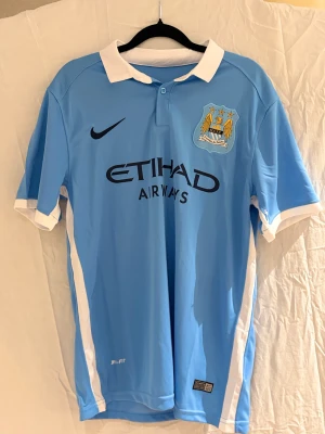 Manchester City Kevin De Bruyne tröja #17 - Snygg Manchester City matchtröja med Kevin De Bruyne och nummer 17 på ryggen. Tröjan är ljusblå med vit krage och vita detaljer vid ärmslut, tillverkad i ventilerande Dri-Fit material. Klassisk klubbmärke på bröstet och svart Nike-logga.