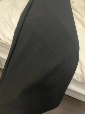 Svarta kostymbyxor med raka ben - Snygga svarta kostymbyxor med klassisk rak passform och midja med knappstängning. Byxorna har bälteshällor och sidfickor, vilket ger en stilren och clean look. Materialet känns mjukt och har en lätt stretch för extra komfort.helt ny