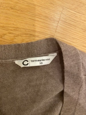 Beige omlottkofta i merinoull XS - Säljer en beige omlottkofta i 100% merinoull från Cubus. Koftan har långa ärmar, v-ringning och knytband i midjan för en snygg passform. Perfekt att slänga på sig under kyliga dagar och supermjuk mot huden.