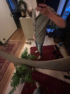 Grå kofta med huva och knappar - Snygg grå kofta med huva och svarta knappar framtill. Tröjan är stickad i mjukt material och har långa ärmar med ribbade muddar. Perfekt för dig som gillar chill och enkel stil. Passar dig som vill ha en normal passform och gillar klassiska detaljer.