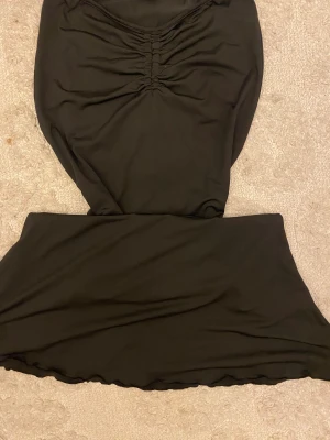 Svart kortkjol med rynkdetalj - Snygg svart kortkjol med rynkade detaljer framtill som ger en cool och trendig look. Kjolen har en enkel design med lätt utsvängd form och är gjord i ett mjukt syntetmaterial som sitter skönt. Perfekt för dig som gillar minimalistisk stil.