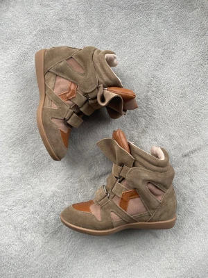 Isabel Marants Khaki  - Unika höga sneakers i brun mocka och skinn med coola paneler och flera breda kardborreband. Snygg plattformssula och rund tå, samt detaljer i ljusbrunt skinn på tån och plösen. Perfekt för dig som gillar statement-skor med streetkänsla.