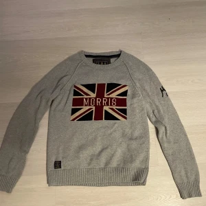 Grå tröja från Morris  - Säljer en stilren grå tröja från Morris med ett stort Union Jack-motiv och texten 'Morris' på bröstet. Tröjan har långa ärmar och ribbade muddar vid ärmslut och nederkant. Perfekt för en klassisk look!