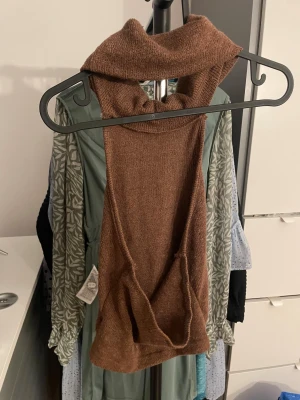 Brun stickad krage/huva - Säljer en brun stickad krage/huva i mjukt material. Perfekt att dra över huvudet för extra värme under jackan. Den har en hög polokrage och är i en enkel, stilren design utan detaljer. Passar perfekt för kalla dagar.