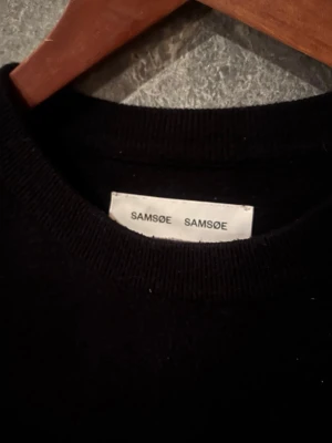 Stickad samsøe samsøe  - En klassisk svart stickad samsøe samsøe tröja med rund hals och långa ärmar. Tröjan har en enkel och stilren design som passar perfekt till många olika outfits. Materialet ser mjukt och bekvämt ut, perfekt för kyligare dagar.