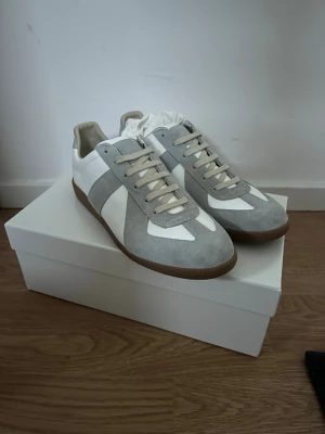 Maison margiela  - Snygga sneakers i vitt och ljusgrått med ovandel i mocka och skinn. Klassisk design med snörning och platt sula i gummi. Perfekta för dig som gillar stilrena och tidlösa sneakers. Märket Maison Margiela väldigt fina o sköna skor passar perfekt inför kommande årstider våren och sommaren väldigt stiliga och passar med allt. PRISET KAN DISKUTERAS:)