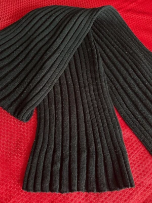 Svart ribbstickad halsduk - En svart ribbstickad halsduk med breda ränder. Halsduken är mjuk och har en klassisk, tidlös design som passar perfekt till kalla dagar. Materialet ser ut att vara stickat, vilket ger en mysig känsla och extra värme.