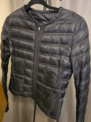 Moncler "Lissy giubbotto" -  lätt dunjacka med fickor - Moncler "Lissy giubbotto" - Snygg svart dunjacka med quiltat mönster och fyra framfickor. Jackan har rund halsringning och dragkedja framtill. Materialet är glansigt och lätt, perfekt för kalla vinterdagar. Enkel och stilren design som passar till det mesta. Som ny!