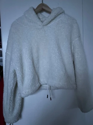 Vit fluffig hoodie med dragsko - Mysig vit hoodie i supermjukt, fluffigt material. Hoodien har huva och dragsko i nederkanten för en avslappnad och trendig look. Perfekt för dig som gillar oversized och comfy vibes.