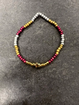 Färgglatt pärlarmband med stjärna storlek M  - Armband med pärlor i guld, silver och röd samt en guldfärgad stjärna i mitten. 