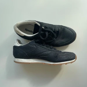 Svarta Reebok sneakers med ormskinnsmönster - Säljer ett par svarta Reebok sneakers med coolt ormskinnsmönster. Skriv om ni har frågor!🖤