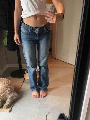 Blå raka jeans i klassisk modell - Säljer ett par blå jeans med rak passform och klassisk femficksdesign. Jeansen har en mellanblå tvätt och är tillverkade i bomull, perfekta för en avslappnad och tidlös look. Är 175cm lång 