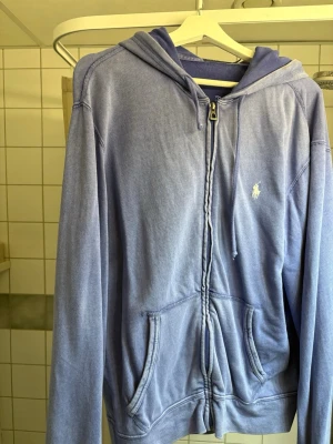 Ljusblå hoodie från Polo Ralph Lauren - Snygg ljuslila tunn hoodie med dragkedja från Polo Ralph Lauren. Hoodien är i nyskick med lite sliten design, urtvättad design