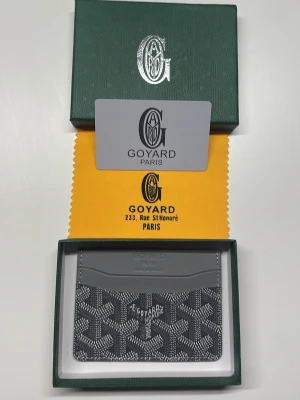 Goy4rd grå plånbok - Snygg grå korthållare i slimmad design. Tillverkad i exklusivt läder med präglad logotyp och flera fack för kort. Kommer med original grön ask och gul putsduk med tryck.