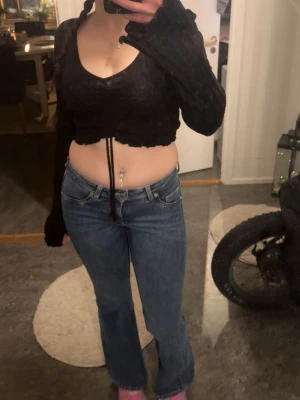 Svart croppad topp med snörning - Säljer en svart croppad topp med långa ärmar och v-ringning. Toppen har snörning framtill som ger en snygg detalj och sitter tight över kroppen. Perfekt för dig som gillar trendiga och edgy plagg.