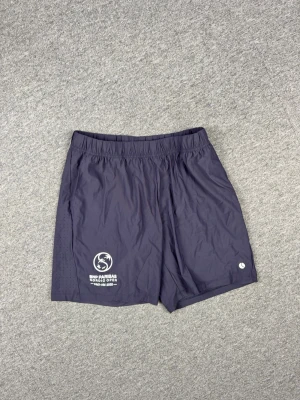 Björneborg Tennis Shorts - Snygga mörkblå shorts från Nordic Open med vitt tryck på vänster ben. Tillverkade i lätt och luftig polyester, perfekta för tennis eller träning. Elastisk midja för skön passform och diskreta ventilationshål på sidorna.