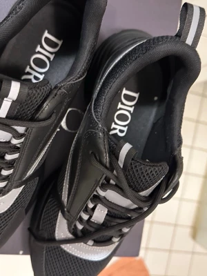 Diorb22 pris kan diskuteras  - Snygga svarta Dior sneakers med cool design i både mesh och läder. Skorna har gråa detaljer, tjock sula och logga på sidan samt innersulan. Perfekta för dig som vill ha en exklusiv och trendig look. Skosnören i svart och praktisk hälflik för enkel påtagning.