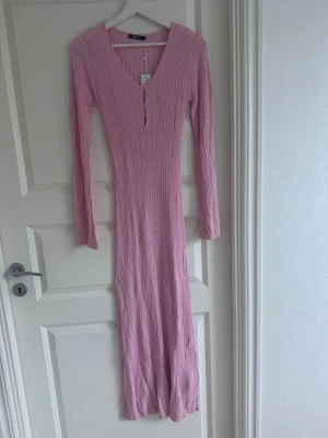 Rosa ribbad långklänning med v-ringning - Långärmad rosa långklänning med ribbad struktur och v-ringning. Klänningen har en smickrande slim passform och är tillverkad i ett mjukt, stretchigt material. Perfekt för dig som gillar en enkel men trendig look.