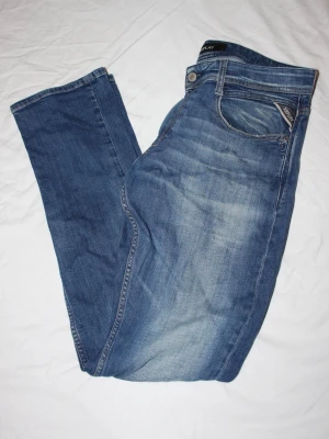 Blå Replay jeans med raka ben - Säljer ett par klassiska blå jeans från Replay med raka ben och snygga slitningar framtill. Jeansen har fem fickor, dragkedja och knappstängning samt Replay-logga på bakfickan och läderpatch i midjan. Perfekta till en avslappnad stil.