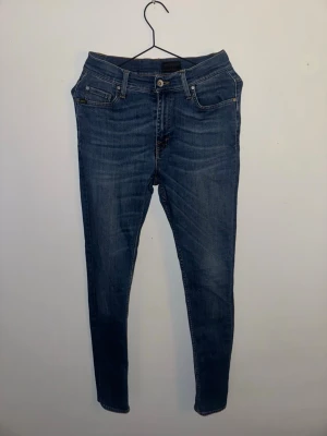 Mörkblå skinny jeans från T/J - Snygga mörkblå skinny jeans från T/J med klassisk femficksdesign och bruna detaljer vid fickorna. Jeansen har en smal passform och är tillverkade i stretchigt denimmaterial för extra komfort. Perfekta för dig som gillar en tajt siluett och stilren look.