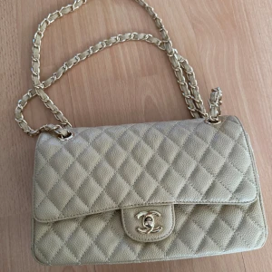 Beige quiltad CC axelväska  - Säljer en beige axelväska med klassiskt quiltat mönster och guldfärgad kedja. Väskan har en ikonisk CC-detalj på locket och är tillverkad i skinn med en lyxig känsla. Perfekt storlek för det viktigaste och snygg att bära crossbody.