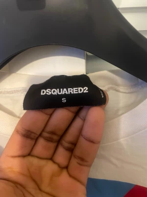 Vit DSQUARED2 T-shirt - Säljer en vit DSQUARED2 t-shirt i storlek S med en stor, färgstark grafisk print på framsidan. Trycket har inslag av blått, rött, gult och svart och texten 'FRESH AFRICA'. T-shirten har rund hals och korta ärmar, tillverkad i mjuk bomull.